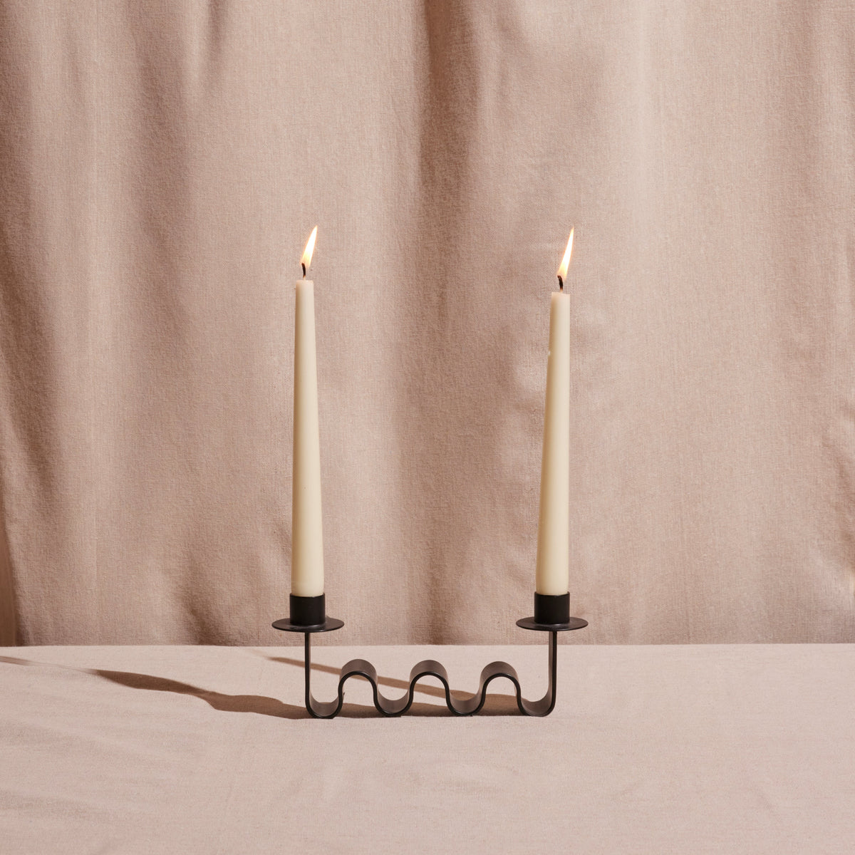 Black metal candle holder with wave forms holding two taper candles