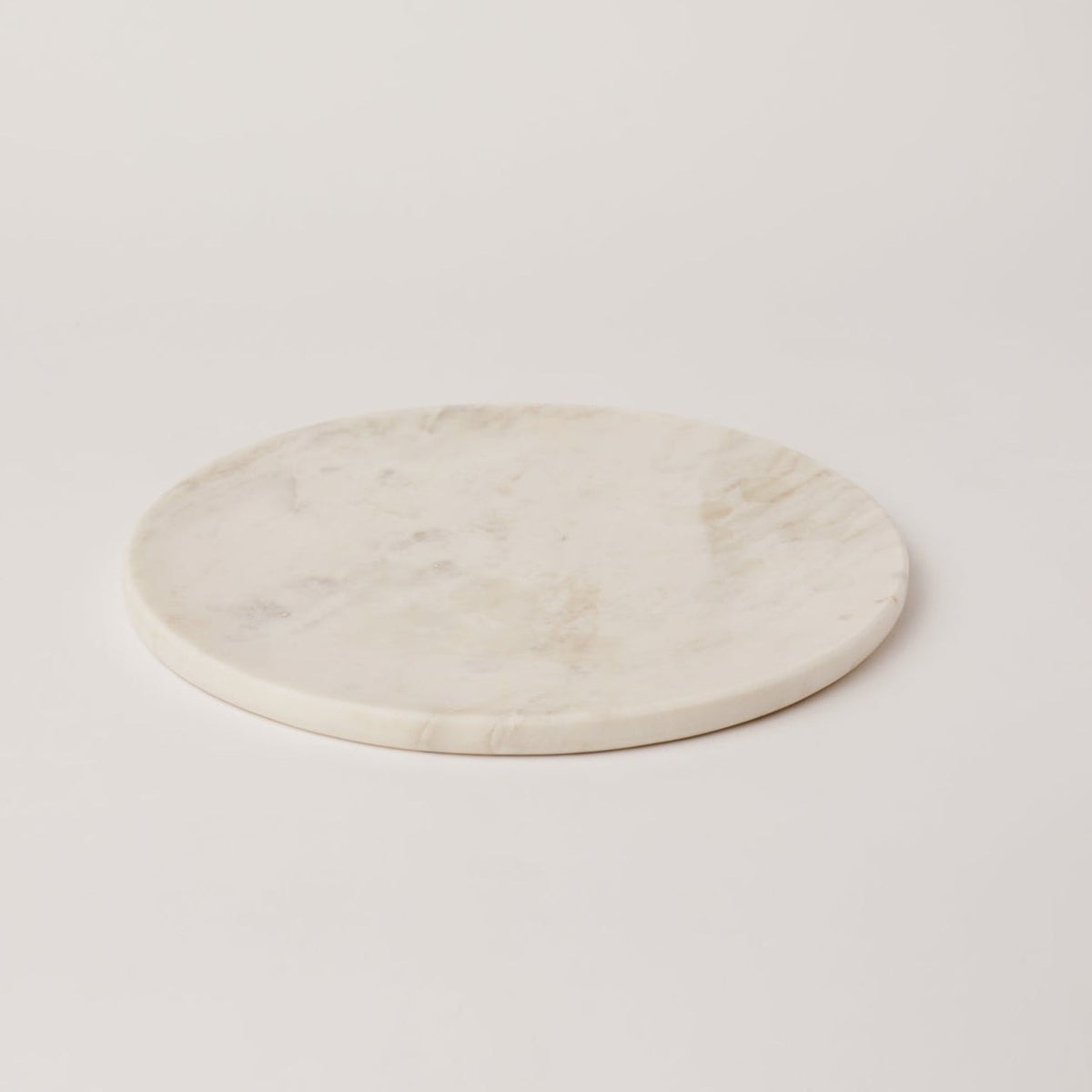 Round white marble platter with grey veining on a table, handmade serveware