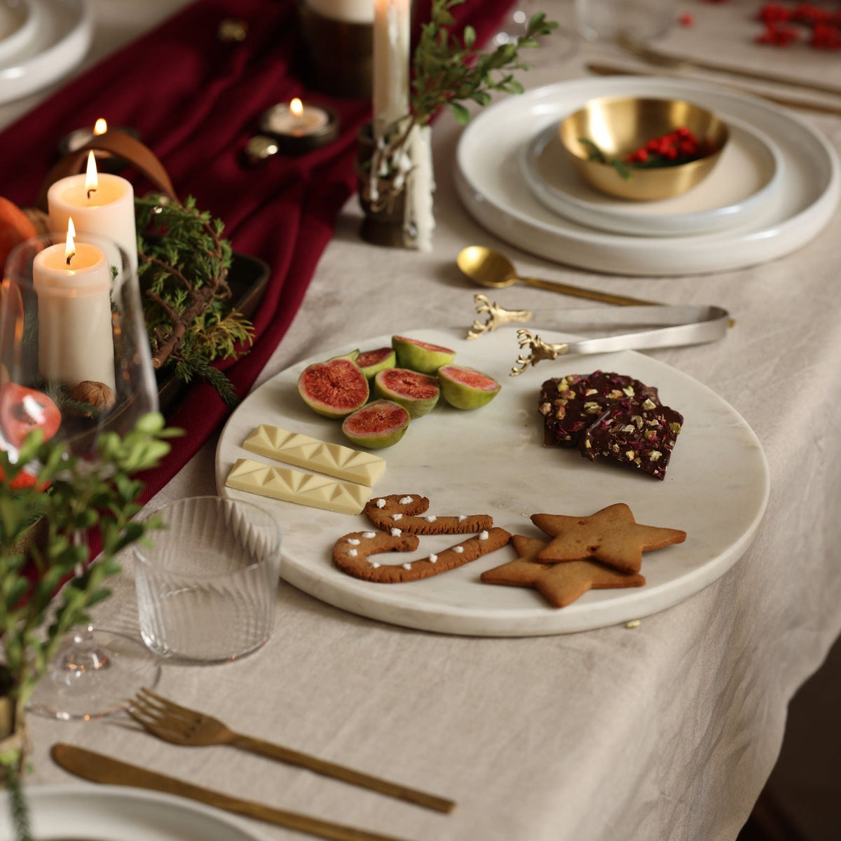White marble plate with figs and cookies on a neutral linen table with candles and brass cutlery